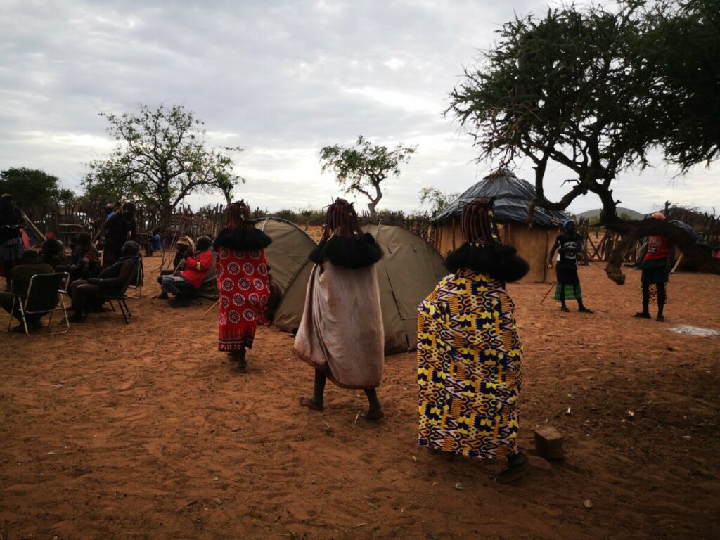 3 vrouwen lopen in een treintje naar de mannen - Himba Gewoontes