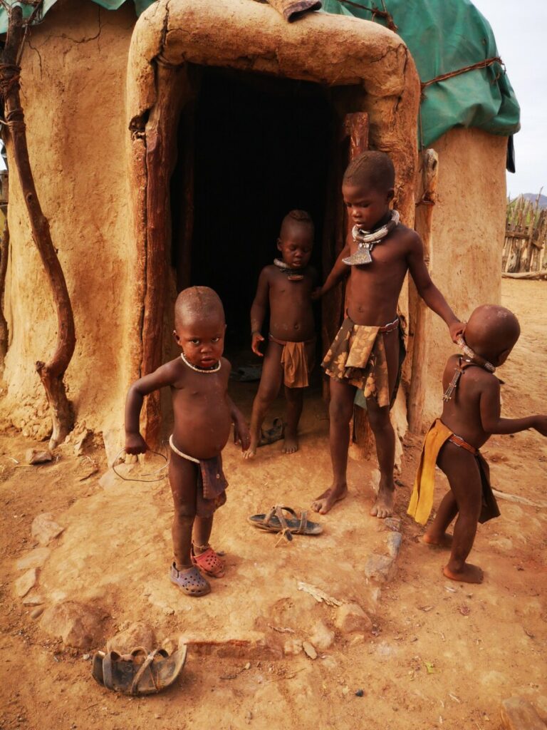 Kinderen spelen voor de ingang van een himba hut